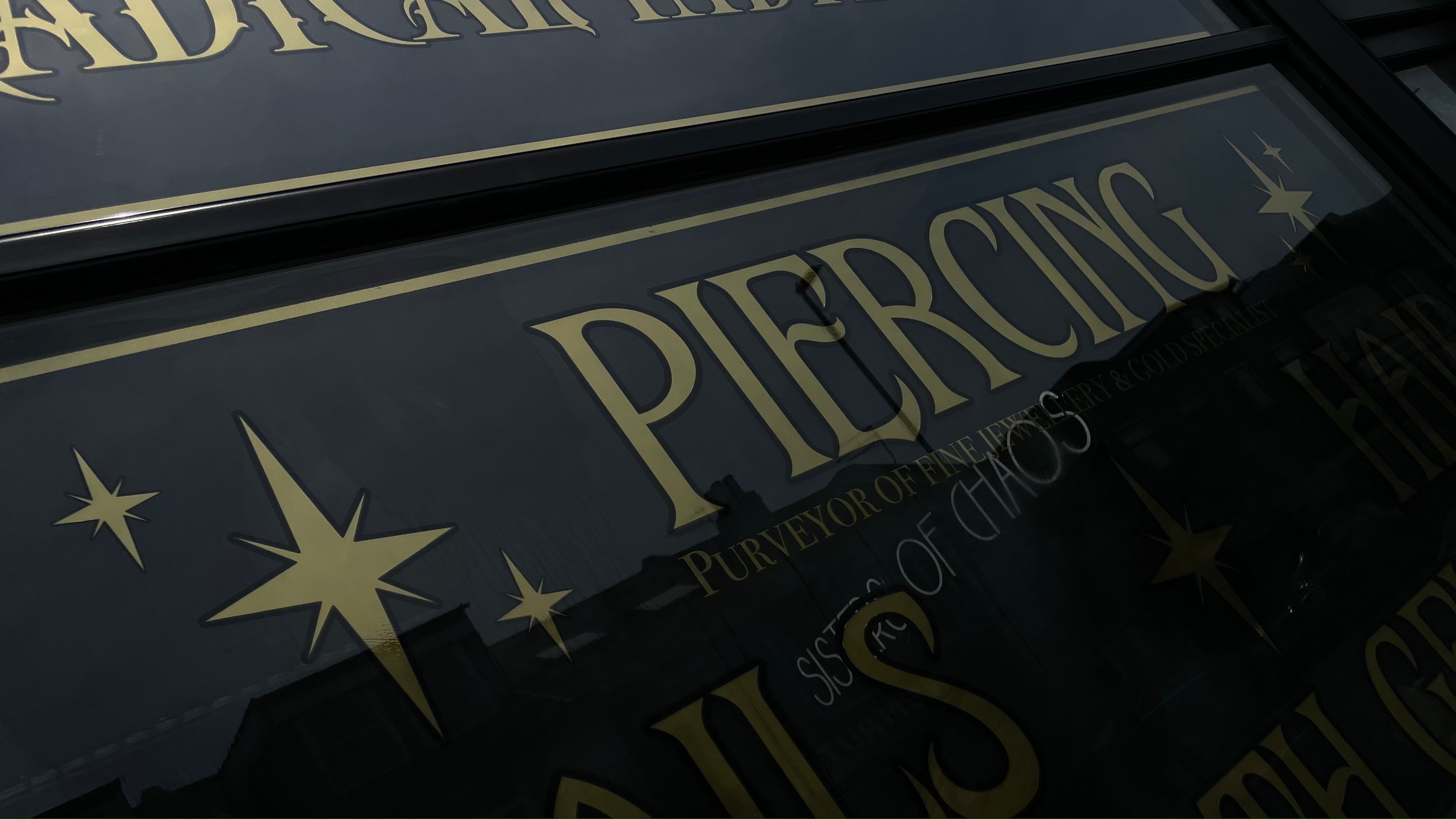 Close-up of a black sign with gold text and star designs, likely for a piercing business.